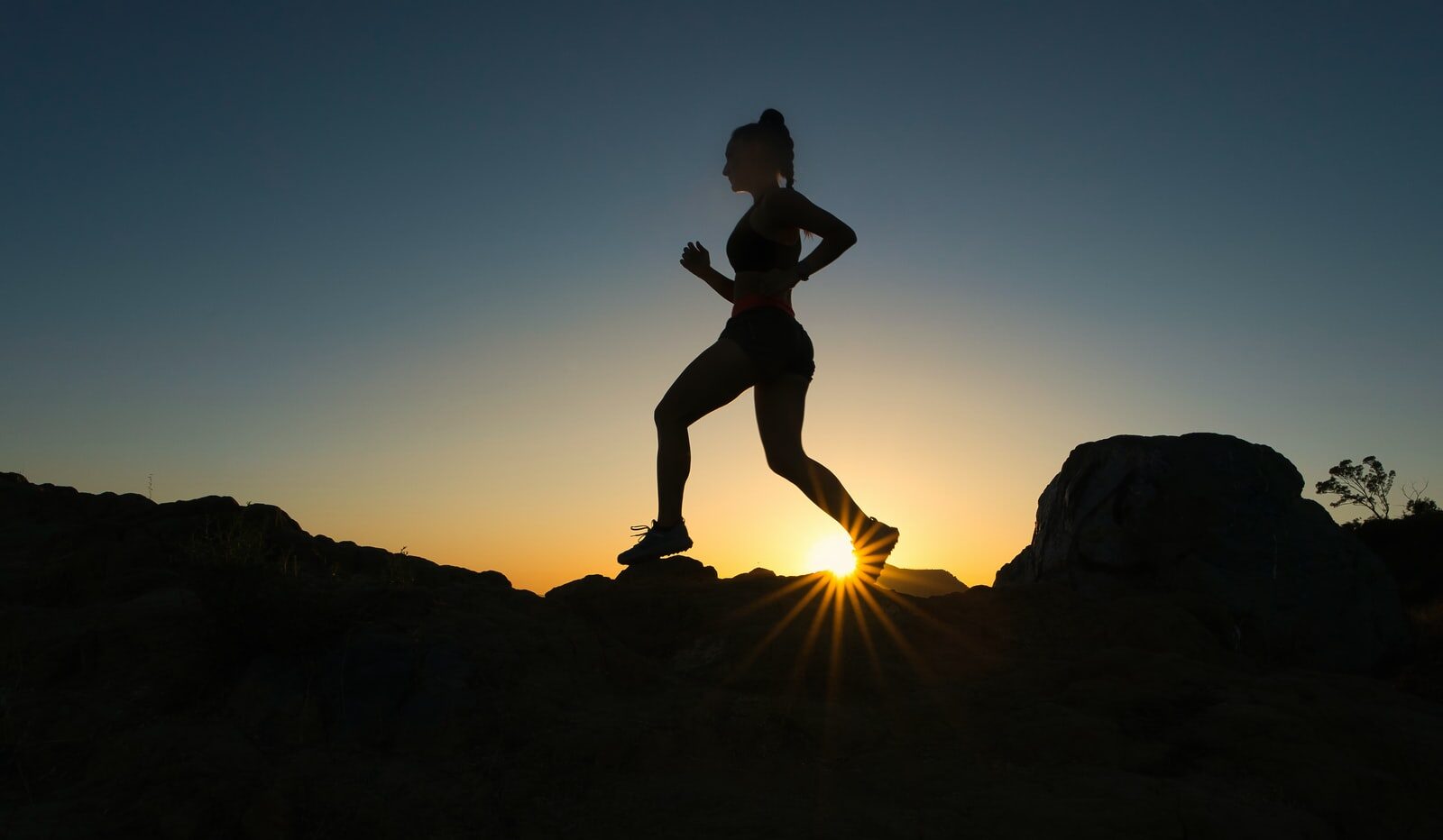 silhouette of man jumping on rocky mountain during sunset