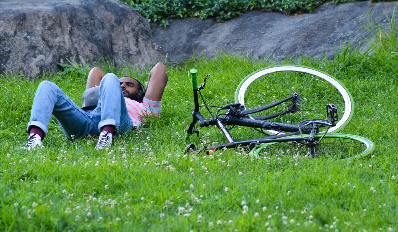 woman in blue denim shorts lying on green grass field beside black and white bicycle during